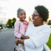 An African American woman carries her three year old daughter on her hip as they walk around their neighborhood in Florida at sunset.